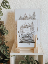 Black and white illustration of a typewriter surrounded with botanicals. The message reads "anthophile." Pair your prints with other illustrations to create a whimsical story of your own.