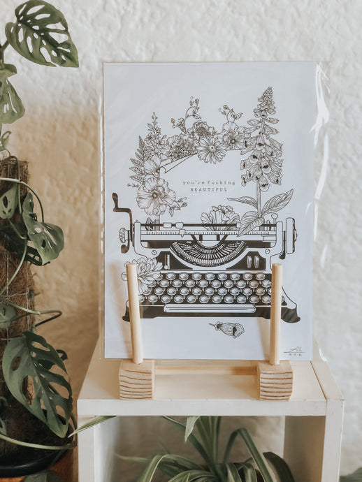 Black and white illustration of a typewriter surrounded with botanicals. The message reads 