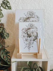 Black and white illustration of the Moon surrounded with botanicals. Pair your prints with other illustrations to create a whimsical story of your own.