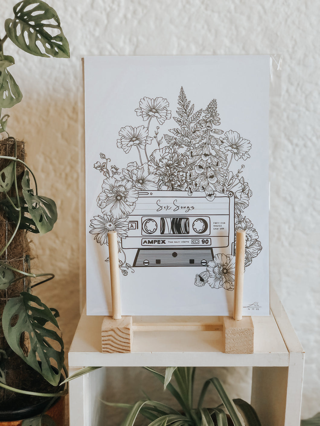 Black and white illustration of a cassette tape surrounded with botanicals. This tape is labelled 