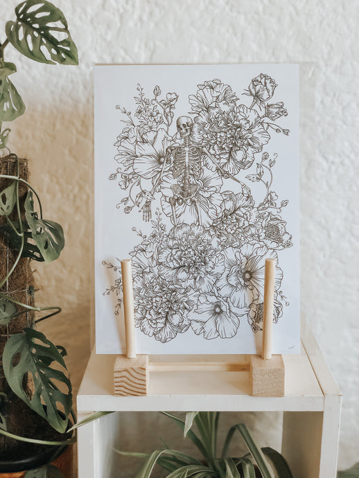 Black and white illustration of a skeleton intricately surrounded with botanicals. Pair your prints with other illustrations to create a whimsical story of your own.
